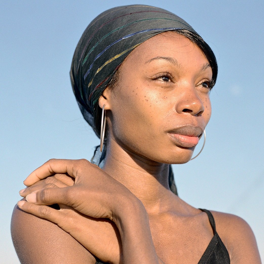 Woman wearing a headscarf and hoop earrings against a clear blue sky.